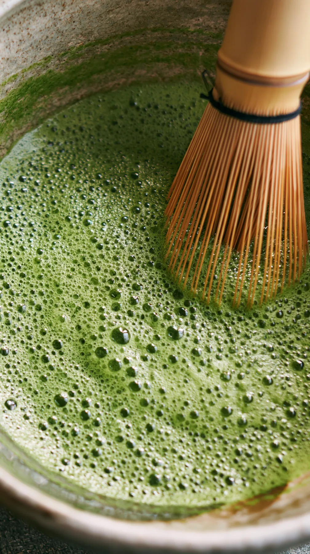 matcha being whisked in a ceramic bowl, bright green foam, overhead, no text, no letters, no logos