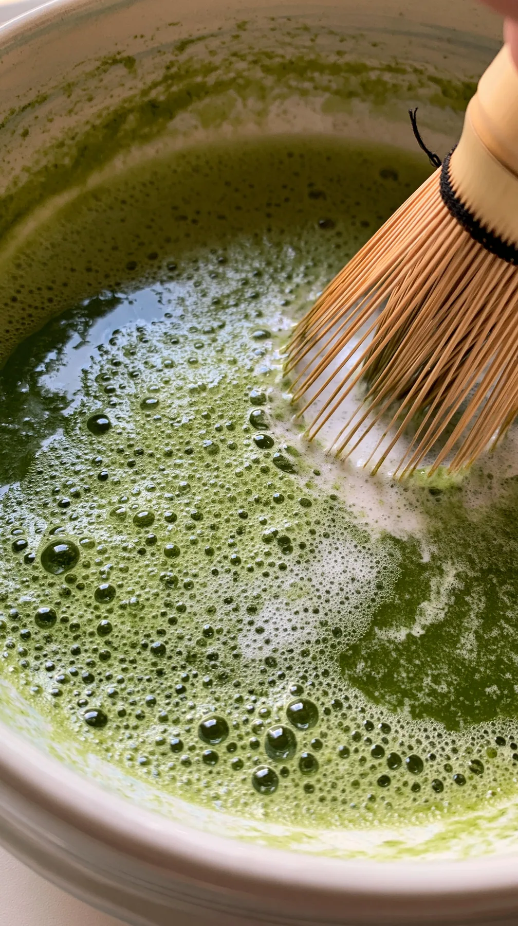 matcha being whisked in a ceramic bowl, bright green foam, overhead, no text, no letters, no logos