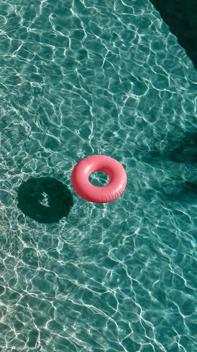 an aerial view of a turquoise pool with a single pink float, hard summer shadows, no text, no letters, no logos