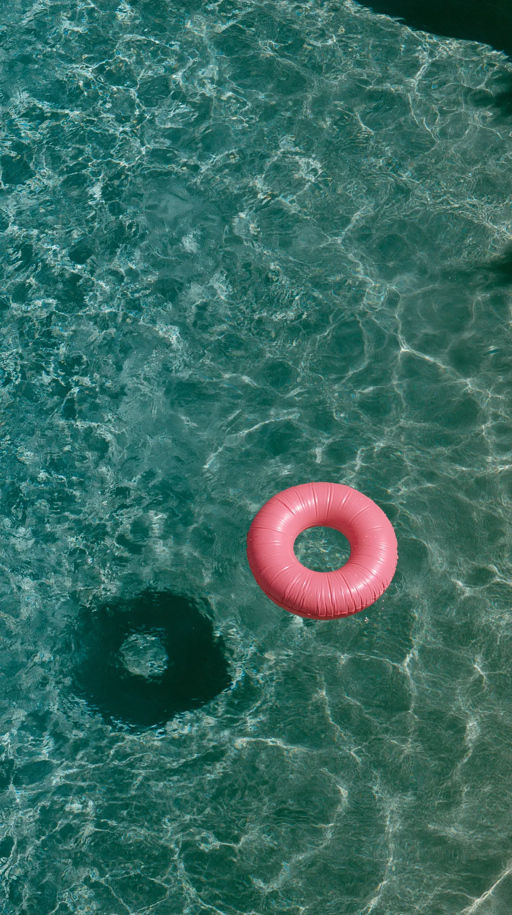 an aerial view of a turquoise pool with a single pink float, hard summer shadows, no text, no letters, no logos