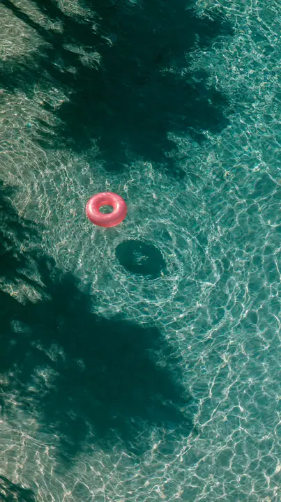 an aerial view of a turquoise pool with a single pink float, hard summer shadows, no text, no letters, no logos