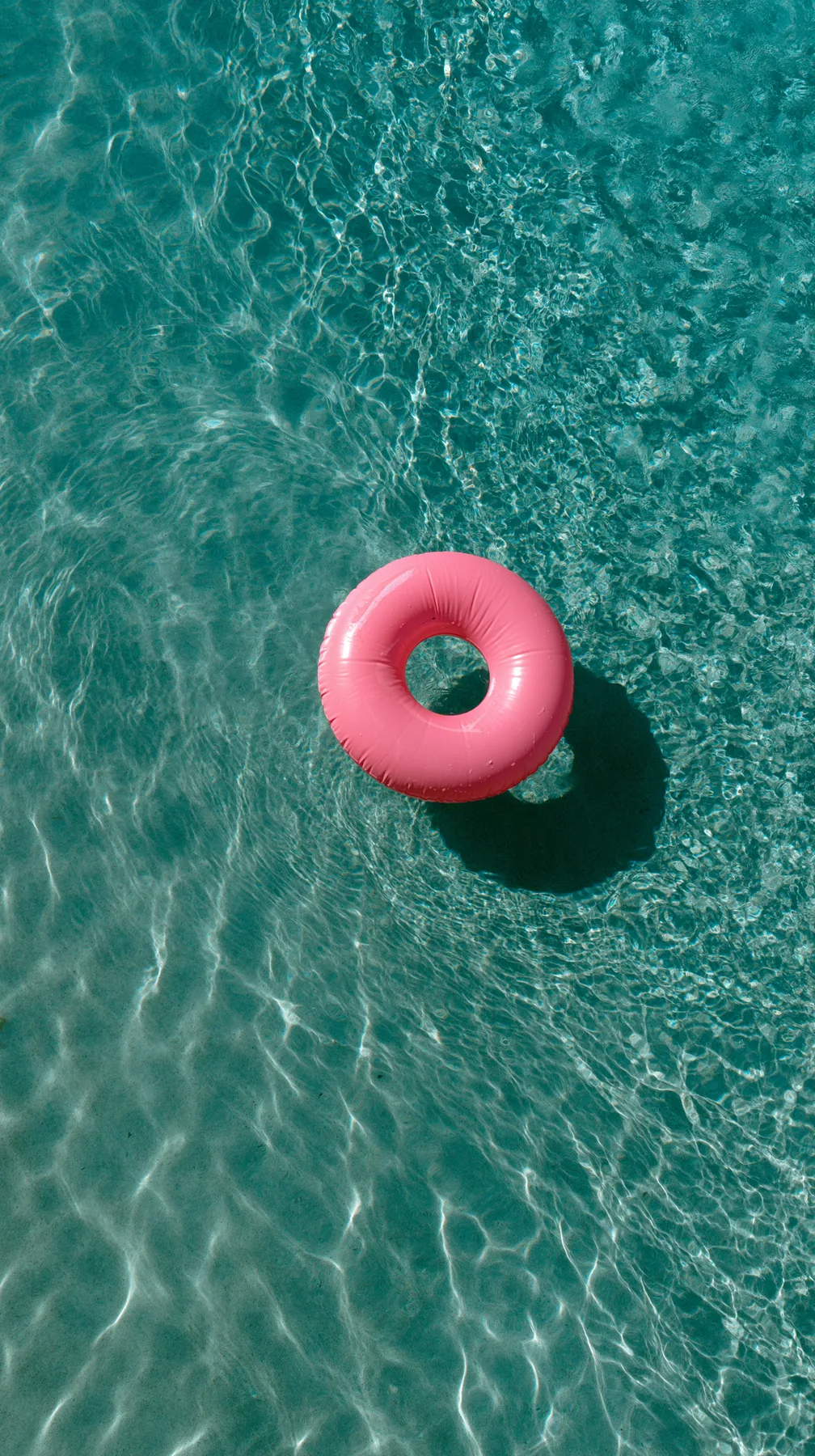 an aerial view of a turquoise pool with a single pink float, hard summer shadows, no text, no letters, no logos