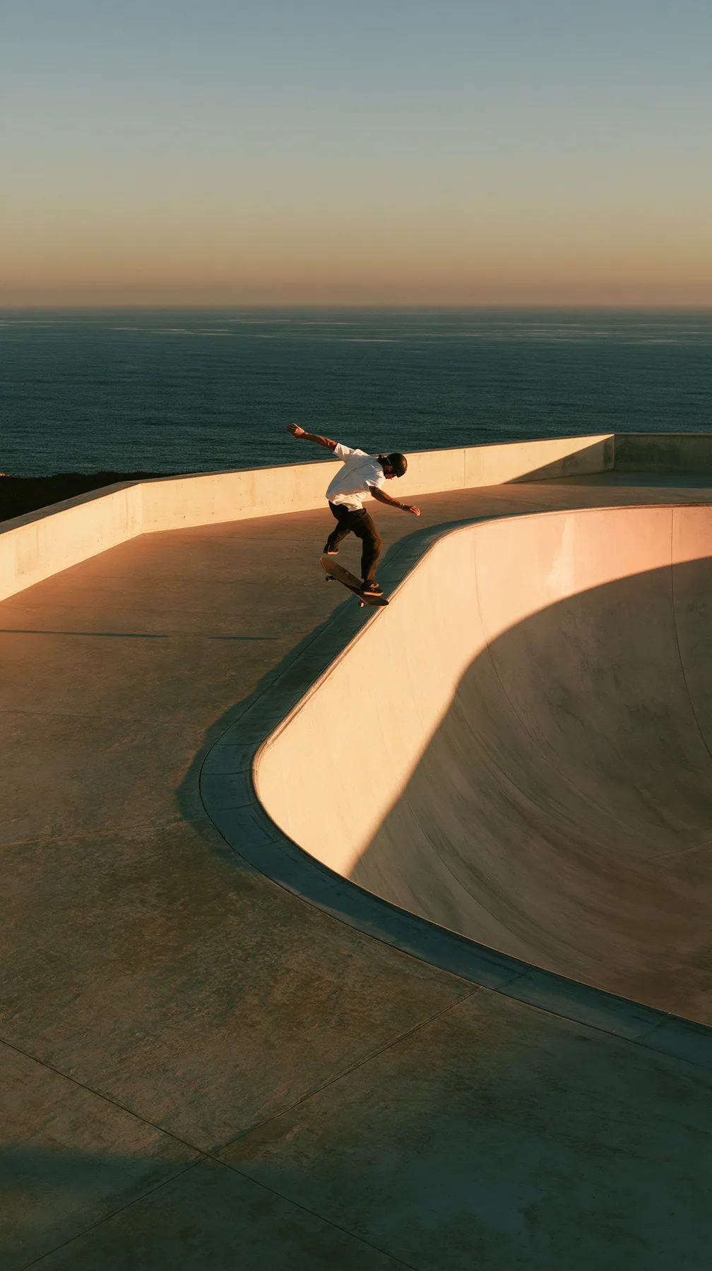 a skateboarder mid-ollie over a pastel concrete ramp at sunset, long shadows, no text, no letters, no logos