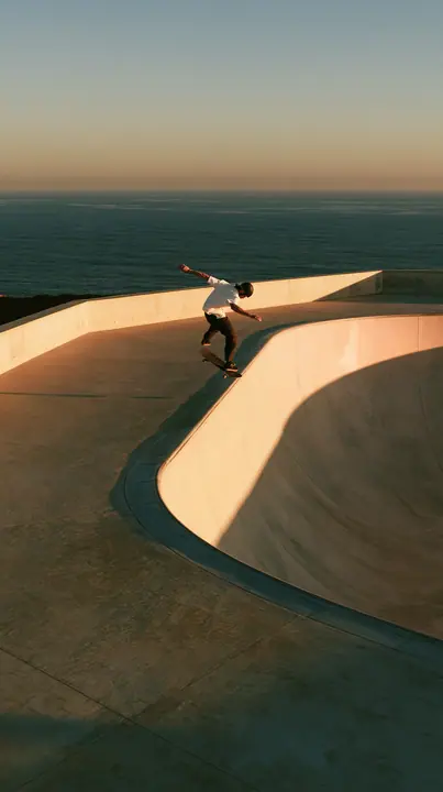 a skateboarder mid-ollie over a pastel concrete ramp at sunset, long shadows, no text, no letters, no logos