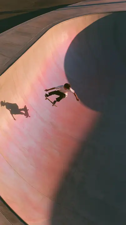 a skateboarder mid-ollie over a pastel concrete ramp at sunset, long shadows, no text, no letters, no logos