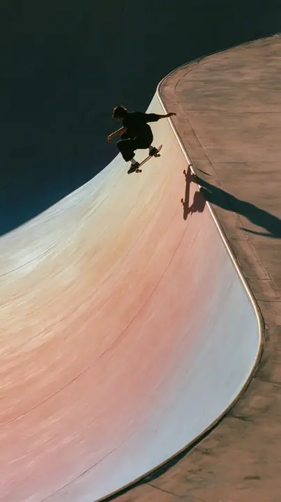 a skateboarder mid-ollie over a pastel concrete ramp at sunset, long shadows, no text, no letters, no logos
