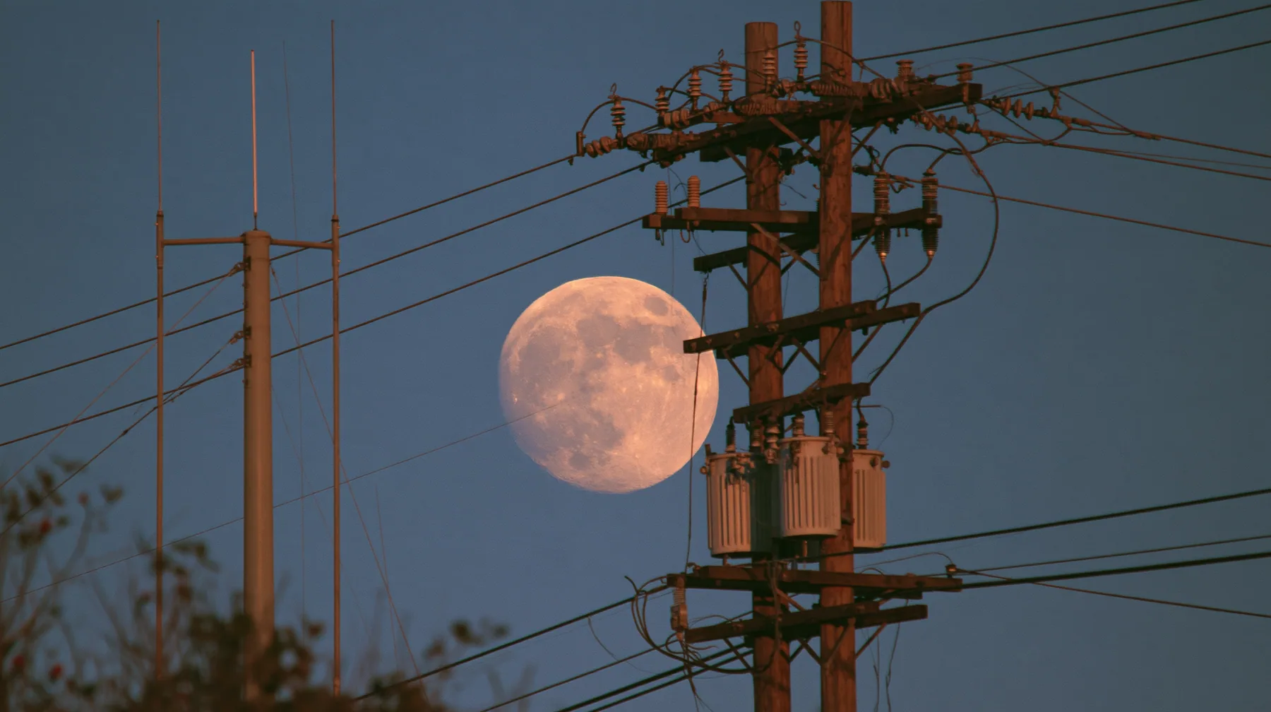a full moon rising behind a power line at dusk, telephoto, crisp, no text, no letters, no logos