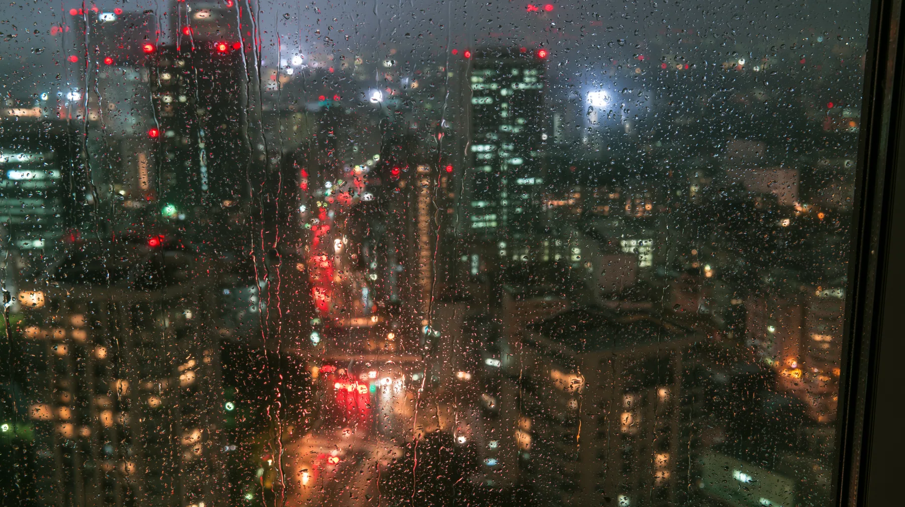a city at night seen through a rain-streaked high-rise window, neon bokeh, moody, no text, no letters, no logos