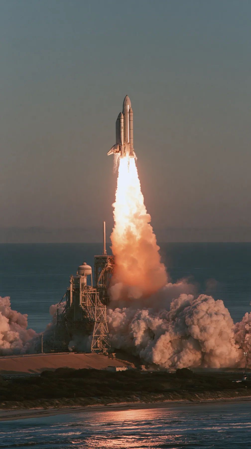 a giant stainless-steel rocket lifting off from a coastal launch tower at dawn, a towering white and orange plume, telephoto documentary photograph, no text, no letters, no logos