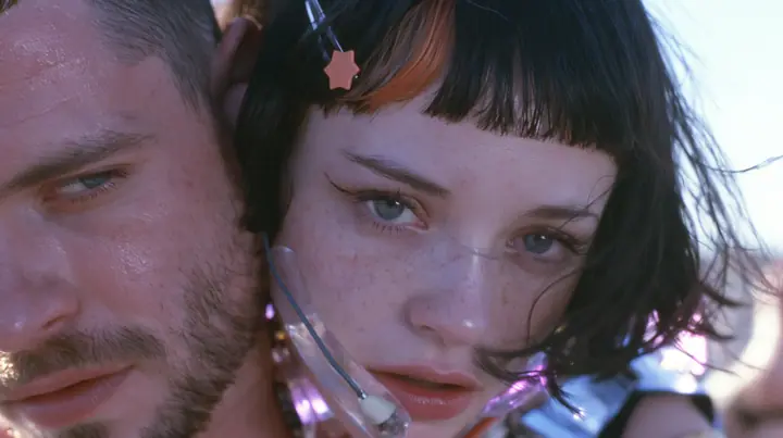 extreme close-up of a Caucasian American woman in her mid-twenties with pale skin and light freckles, a glossy black blunt jaw-length bob with heavy straight bangs and one clay-orange streak through the bangs, a…