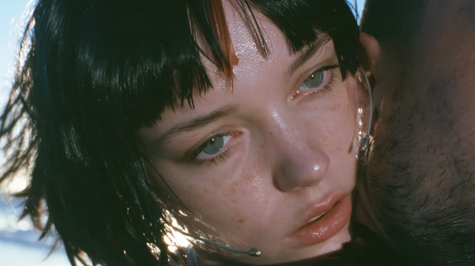 extreme close-up of a Caucasian American woman in her mid-twenties with pale skin and light freckles, a glossy black blunt jaw-length bob with heavy straight bangs and one clay-orange streak through the bangs, a…