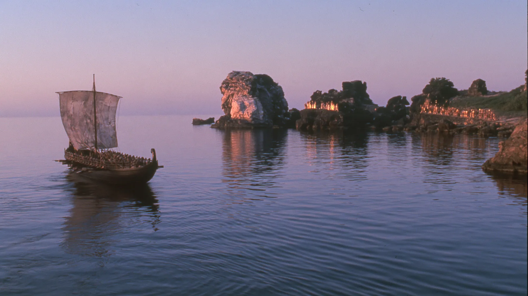 extreme wide shot from behind a long black ancient Greek galley with a single mast, a square sail and two banks of oars on a glassy sea, on the horizon a cluster of black rocks with tiny gold-lit figures of women,…