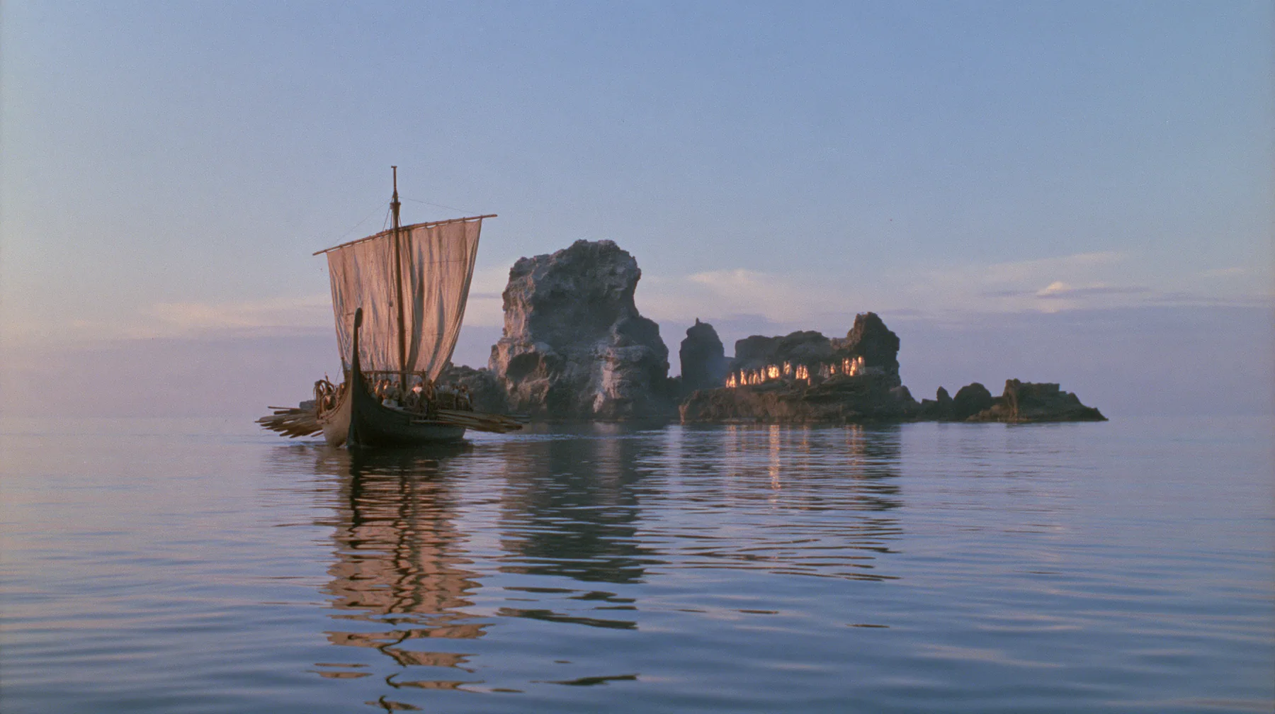 extreme wide shot from behind a long black ancient Greek galley with a single mast, a square sail and two banks of oars on a glassy sea, on the horizon a cluster of black rocks with tiny gold-lit figures of women,…