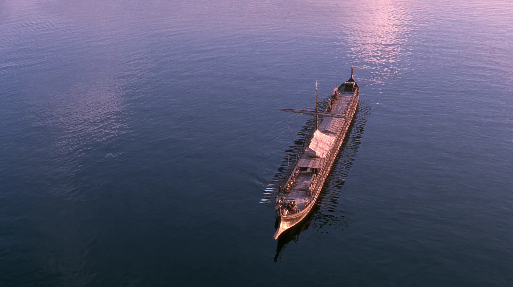 straight-down aerial of a long black ancient Greek galley with a single mast, a square sail and two banks of oars at dusk on a glassy violet sea, the two rows of oars in perfect order like lines on a page, dusk, low…
