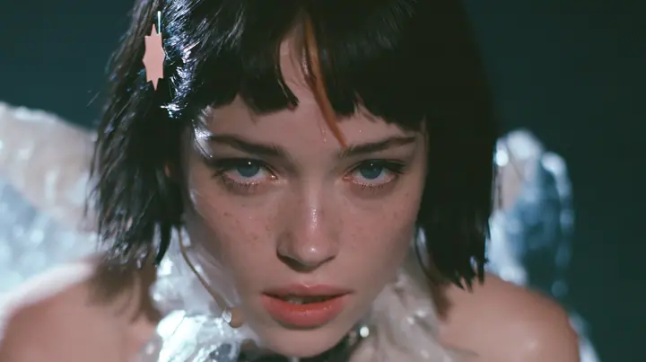 close-up of a Caucasian American woman in her mid-twenties with pale skin and light freckles, a glossy black blunt jaw-length bob with heavy straight bangs and one clay-orange streak through the bangs, a small flat…
