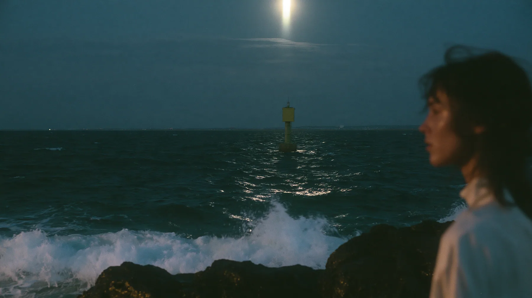 wide shot from beside a woman's bare shoulder on a black sea rock looking out over a dark sea, a navigation buoy bobbing in the middle distance with a blank yellow enamel sign, night, moonlight on a black-teal sea,…