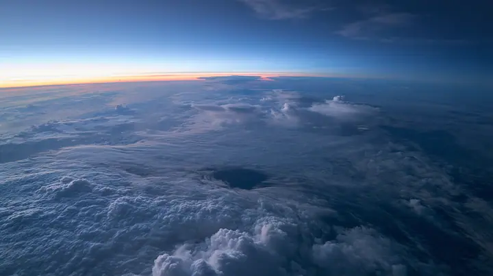 extreme wide aerial photograph from twelve kilometres above a white cloud deck at blue hour, one dark round gap in the clouds far below, the curve of the earth, no text, no letters, no logos