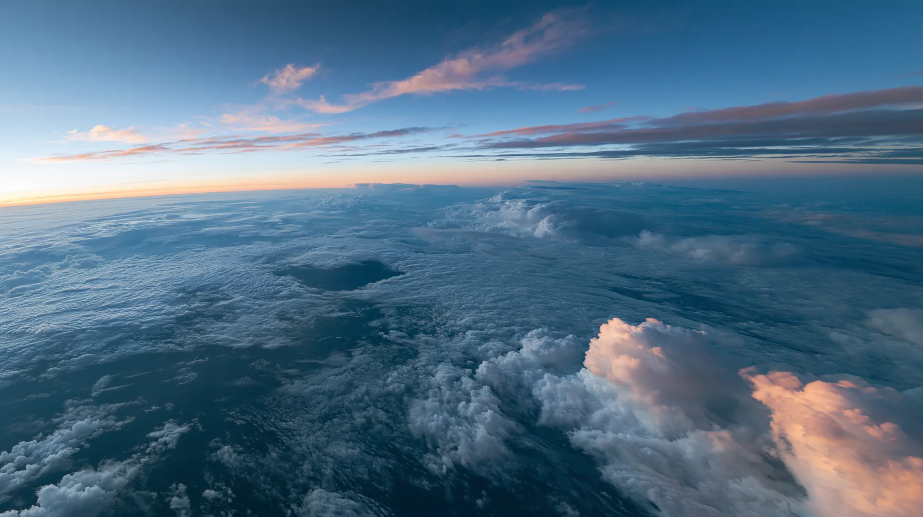 extreme wide aerial photograph from twelve kilometres above a white cloud deck at blue hour, one dark round gap in the clouds far below, the curve of the earth, no text, no letters, no logos