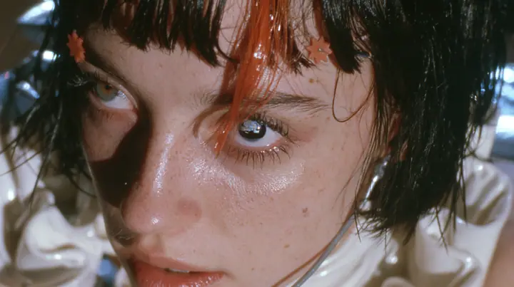 extreme close-up of the right eye of a Caucasian American woman in her mid-twenties with pale skin and light freckles, a glossy black blunt jaw-length bob with heavy straight bangs and one clay-orange streak through…