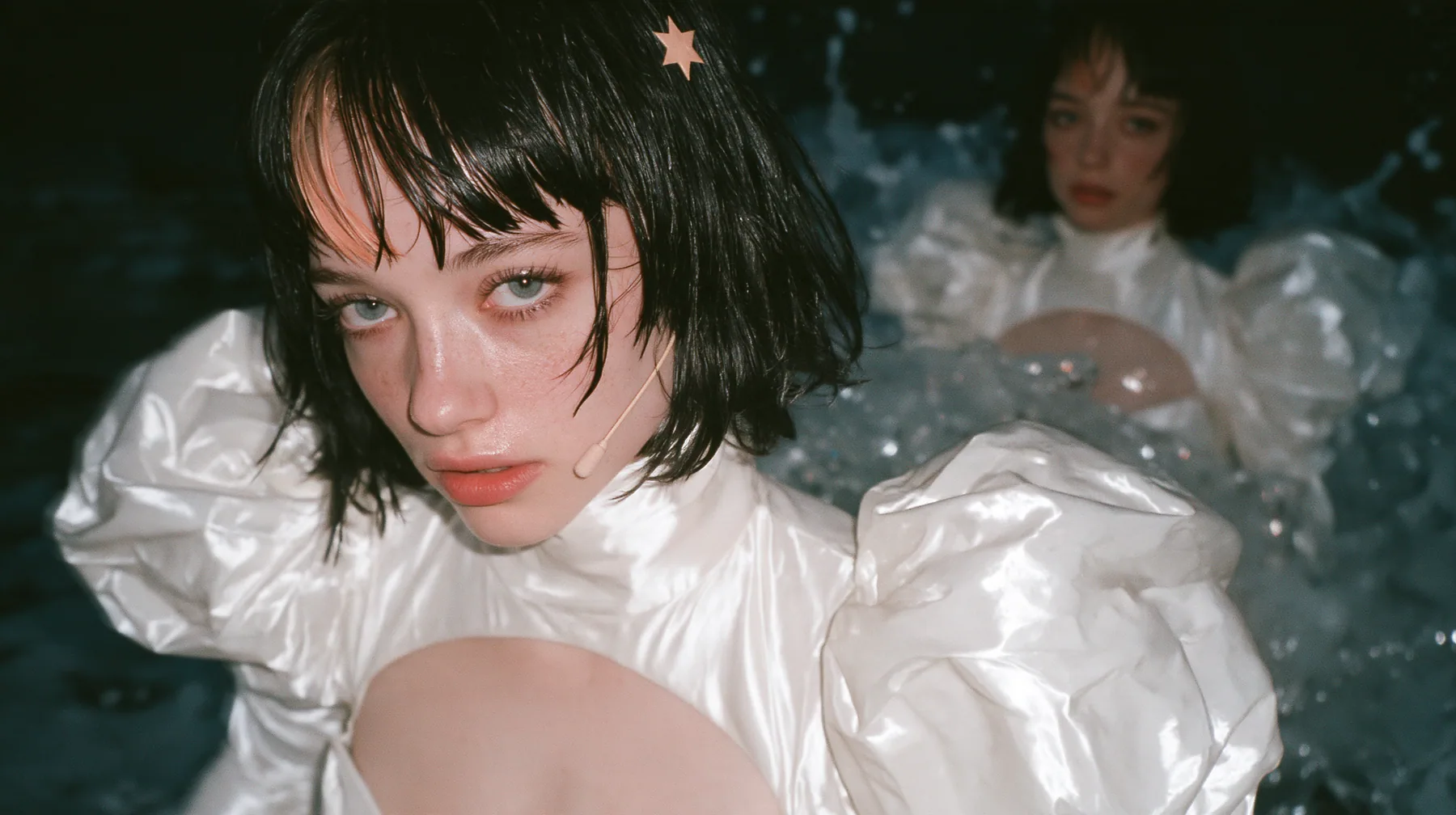 wide shot of a Caucasian American woman in her mid-twenties with pale skin and light freckles, a glossy black blunt jaw-length bob with heavy straight bangs and one clay-orange streak through the bangs, a small flat…