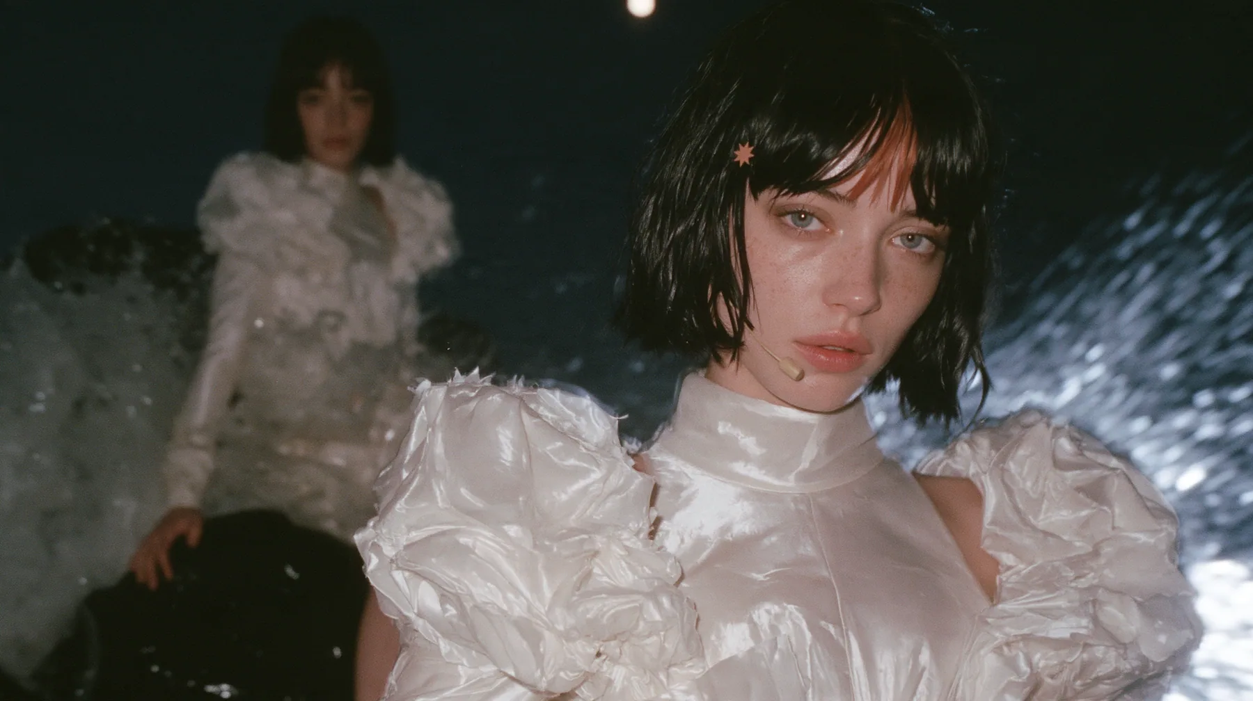 wide shot of a Caucasian American woman in her mid-twenties with pale skin and light freckles, a glossy black blunt jaw-length bob with heavy straight bangs and one clay-orange streak through the bangs, a small flat…