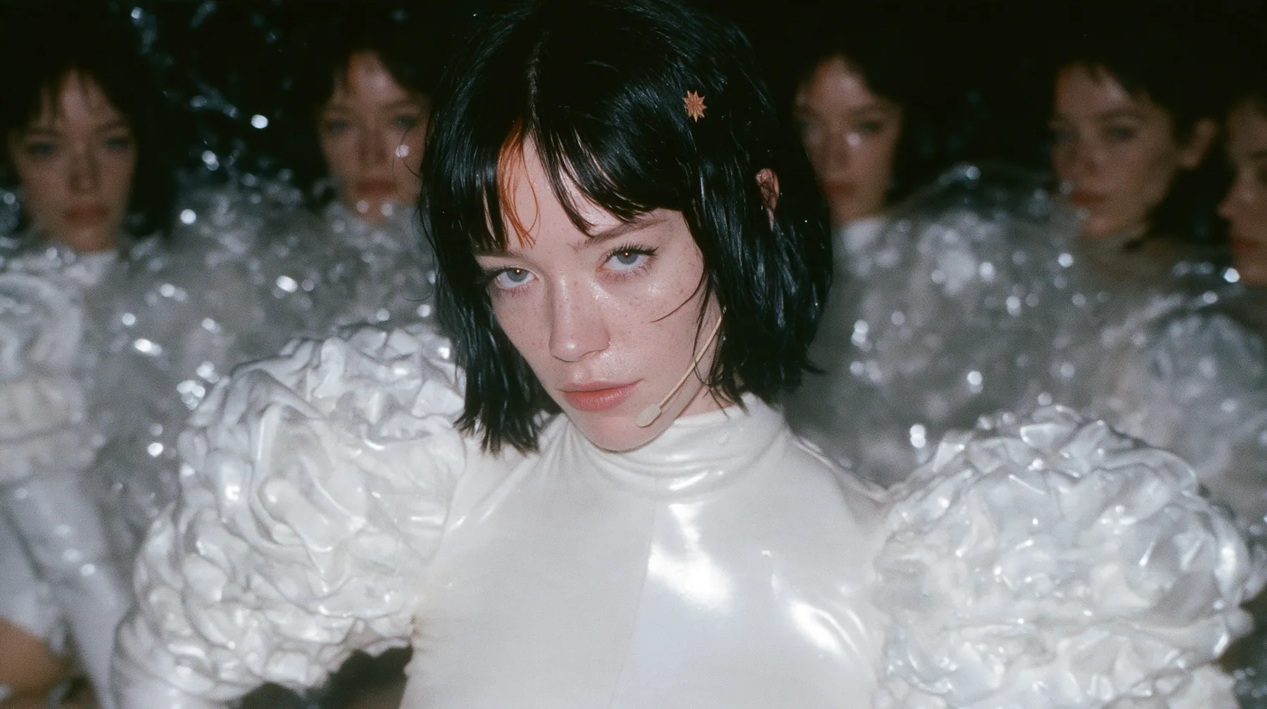 wide shot of a Caucasian American woman in her mid-twenties with pale skin and light freckles, a glossy black blunt jaw-length bob with heavy straight bangs and one clay-orange streak through the bangs, a small flat…