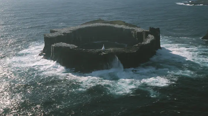 high wide aerial of a ring of black sea stacks covered with hundreds of identical pale women in white gowns, all facing the same direction, night, moonlight on a black-teal sea, silver spray, cinematic 35mm film…