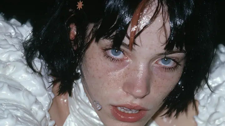 extreme close-up of the lips of a Caucasian American woman in her mid-twenties with pale skin and light freckles, a glossy black blunt jaw-length bob with heavy straight bangs and one clay-orange streak through the…