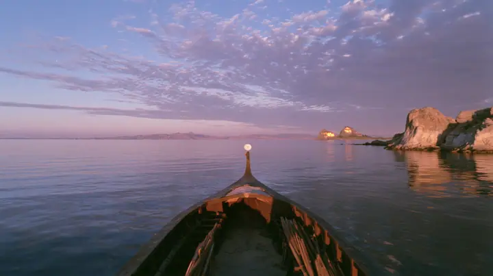 low angle up the mast of a long black ancient Greek galley with a single mast, a square sail and two banks of oars, a small white satellite dish at the top, distant rocks glowing gold on the horizon, dusk, low gold…