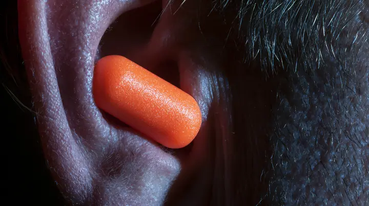 macro photograph of a bright orange foam earplug expanding inside a man's ear, macro product photograph, hard rim light, razor-thin focus, dark background, no text, no letters, no logos