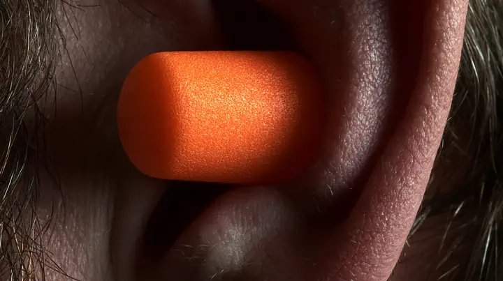 macro photograph of a bright orange foam earplug expanding inside a man's ear, macro product photograph, hard rim light, razor-thin focus, dark background, no text, no letters, no logos