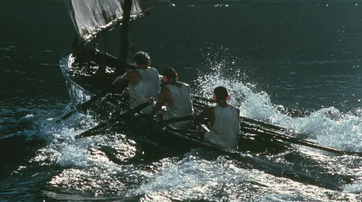 medium close-up over the gunwale of a long black ancient Greek galley with a single mast, a square sail and two banks of oars on a calm moonlit sea, three rowers in undyed linen tunics pulling the oars in time,…