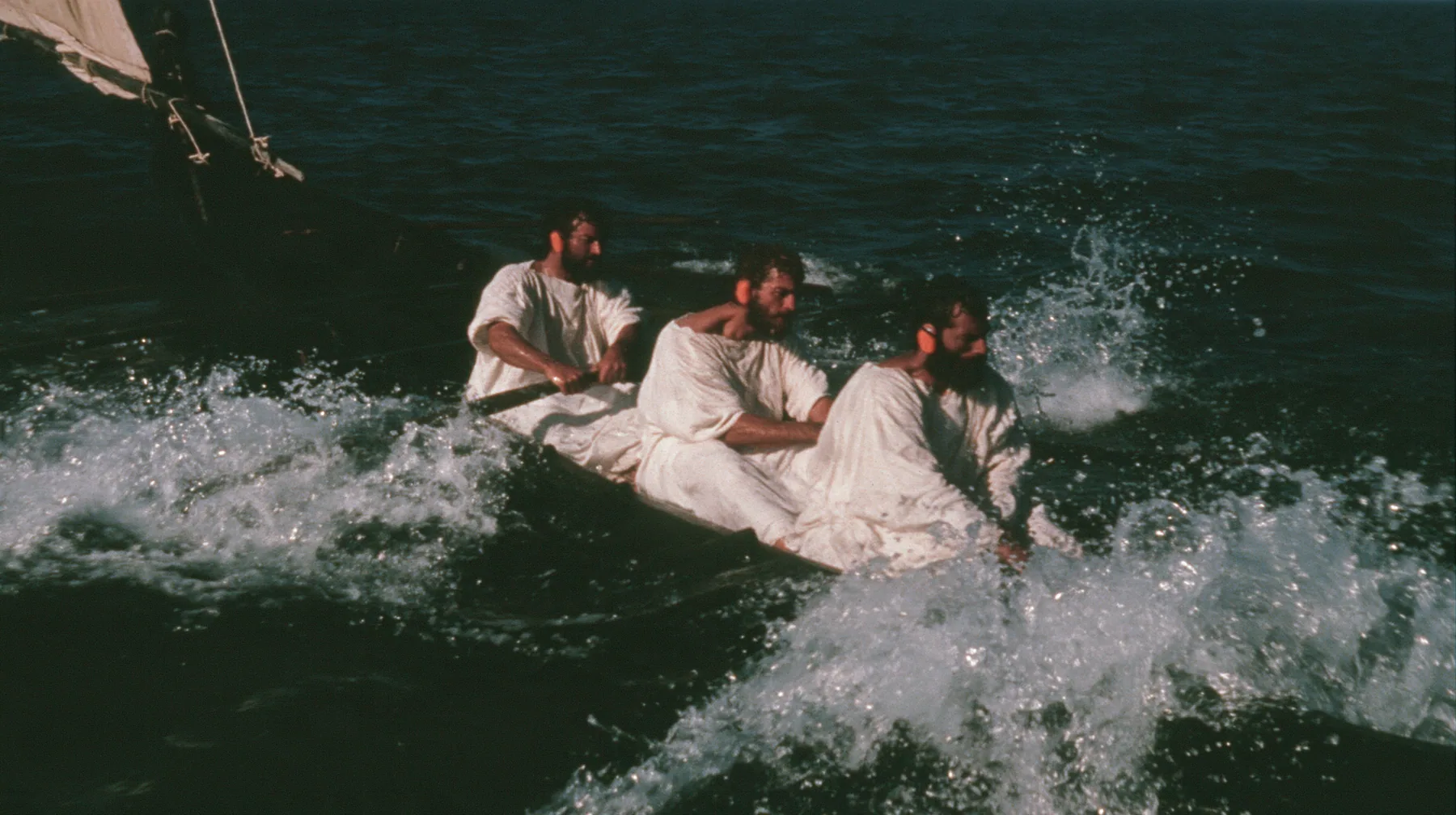 medium close-up over the gunwale of a long black ancient Greek galley with a single mast, a square sail and two banks of oars on a calm moonlit sea, three rowers in undyed linen tunics pulling the oars in time,…