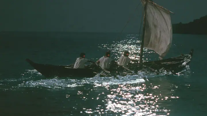 medium close-up over the gunwale of a long black ancient Greek galley with a single mast, a square sail and two banks of oars on a calm moonlit sea, three rowers in undyed linen tunics pulling the oars in time,…