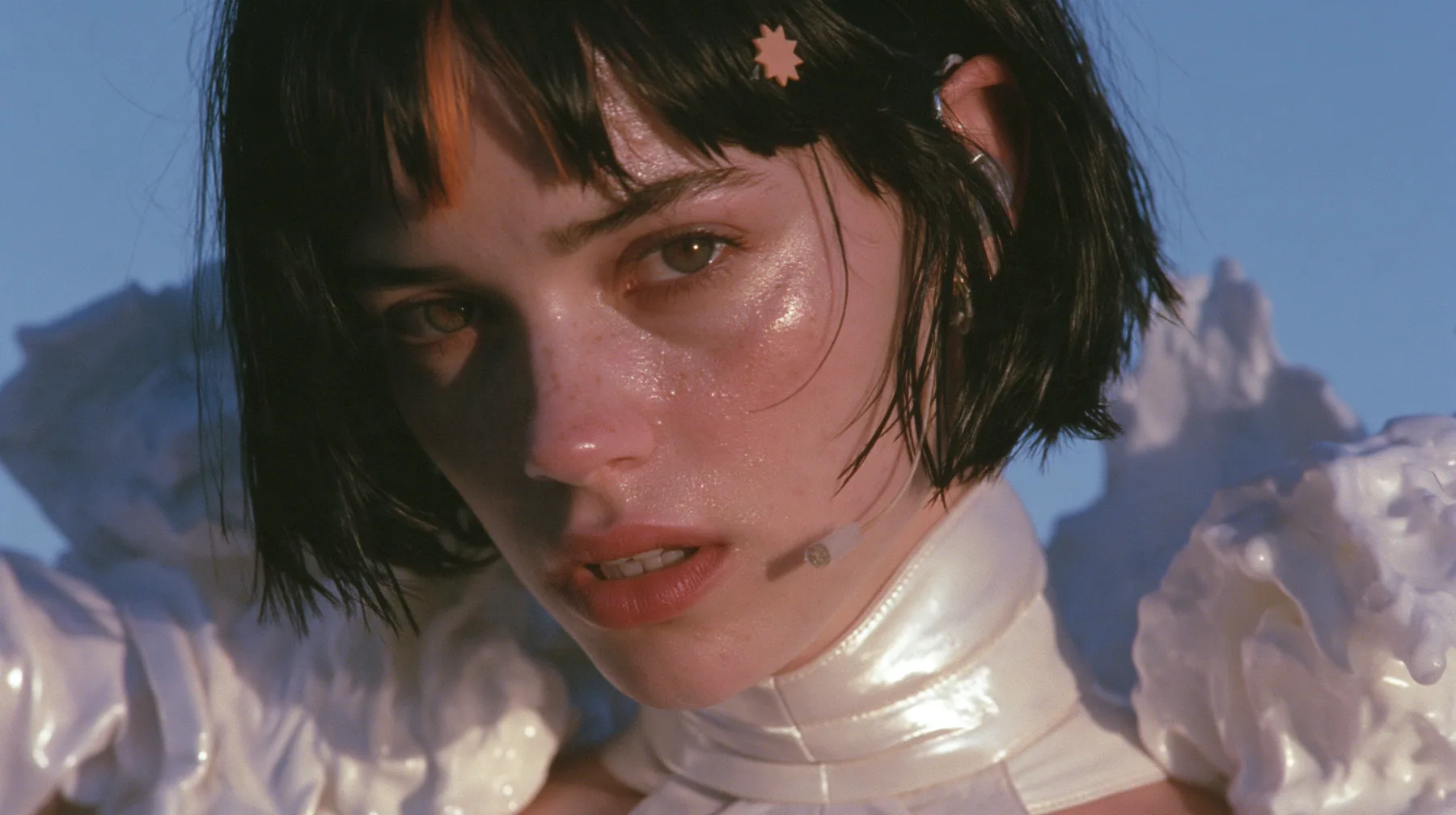 long-lens close-up of a Caucasian American woman in her mid-twenties with pale skin and light freckles, a glossy black blunt jaw-length bob with heavy straight bangs and one clay-orange streak through the bangs, a…