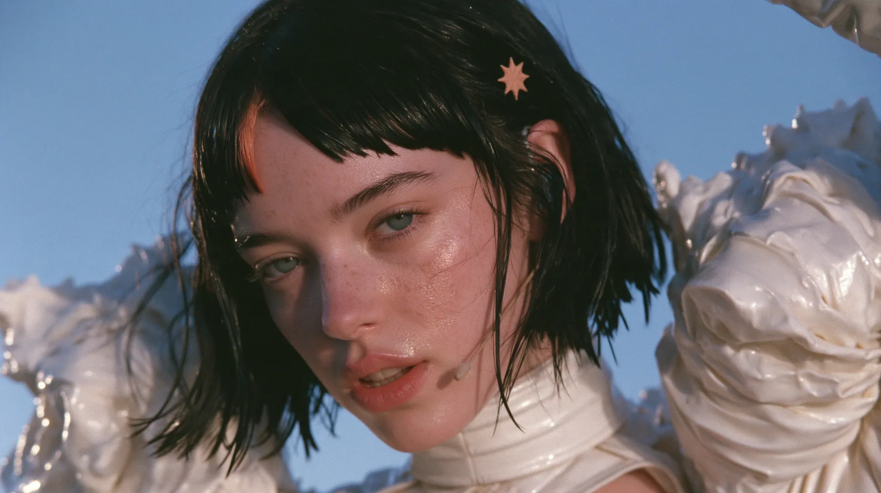 long-lens close-up of a Caucasian American woman in her mid-twenties with pale skin and light freckles, a glossy black blunt jaw-length bob with heavy straight bangs and one clay-orange streak through the bangs, a…