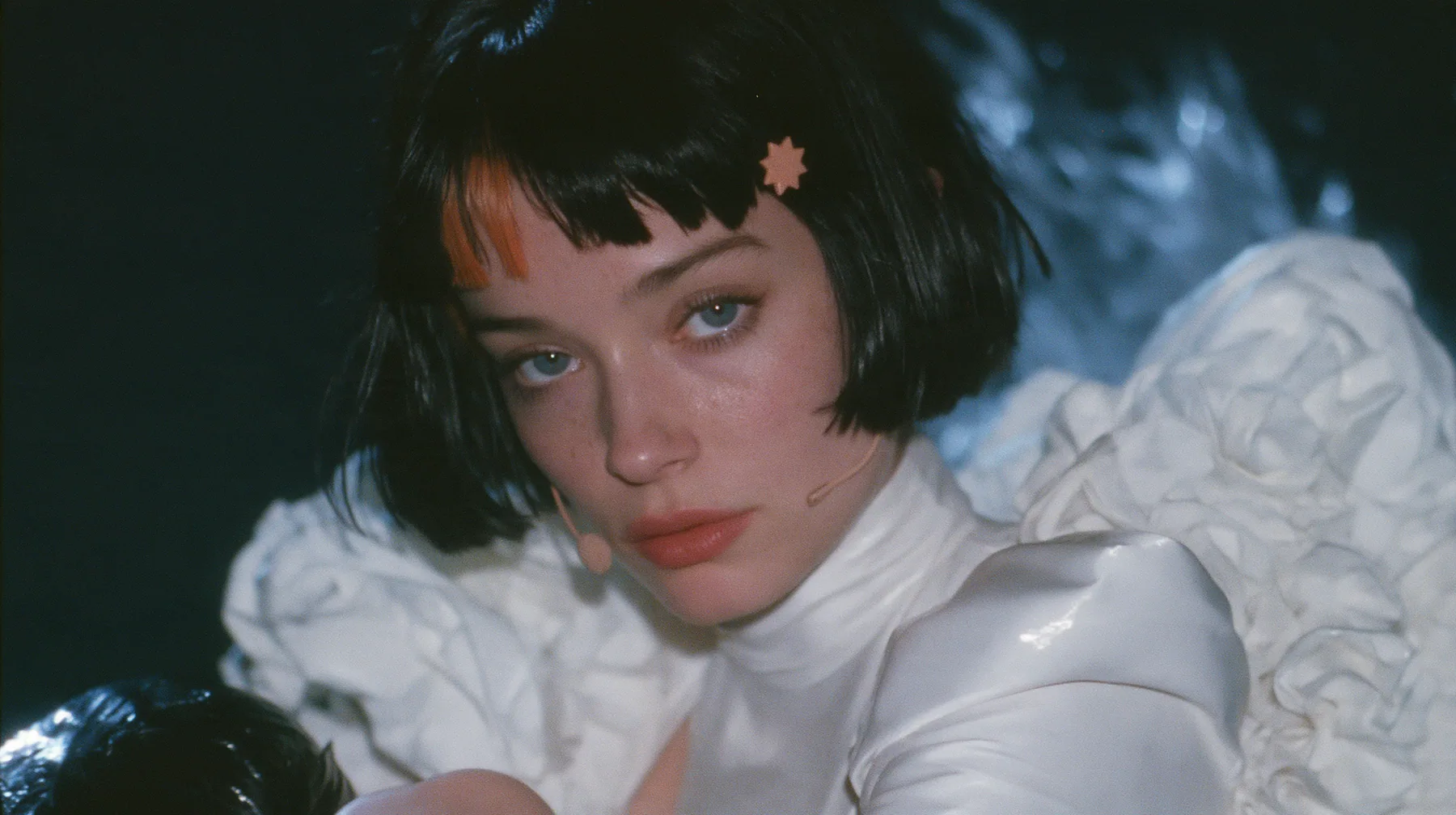 medium close-up of a Caucasian American woman in her mid-twenties with pale skin and light freckles, a glossy black blunt jaw-length bob with heavy straight bangs and one clay-orange streak through the bangs, a small…