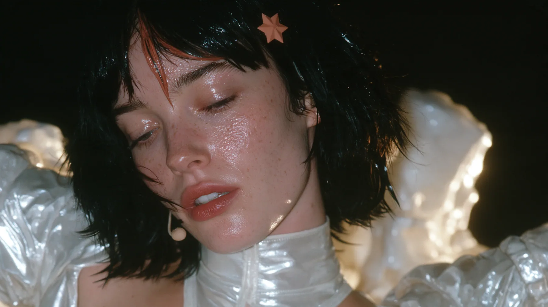 close-up of a Caucasian American woman in her mid-twenties with pale skin and light freckles, a glossy black blunt jaw-length bob with heavy straight bangs and one clay-orange streak through the bangs, a small flat…