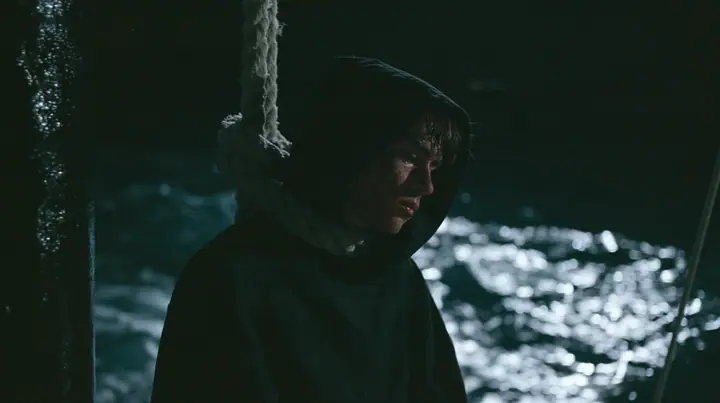 a gaunt young man in a black hoodie tied to the mast of a black ship with thick rope, night, moonlight on a black-teal sea, silver spray, cinematic 35mm film still, anamorphic, fine grain, no text, no letters, no logos