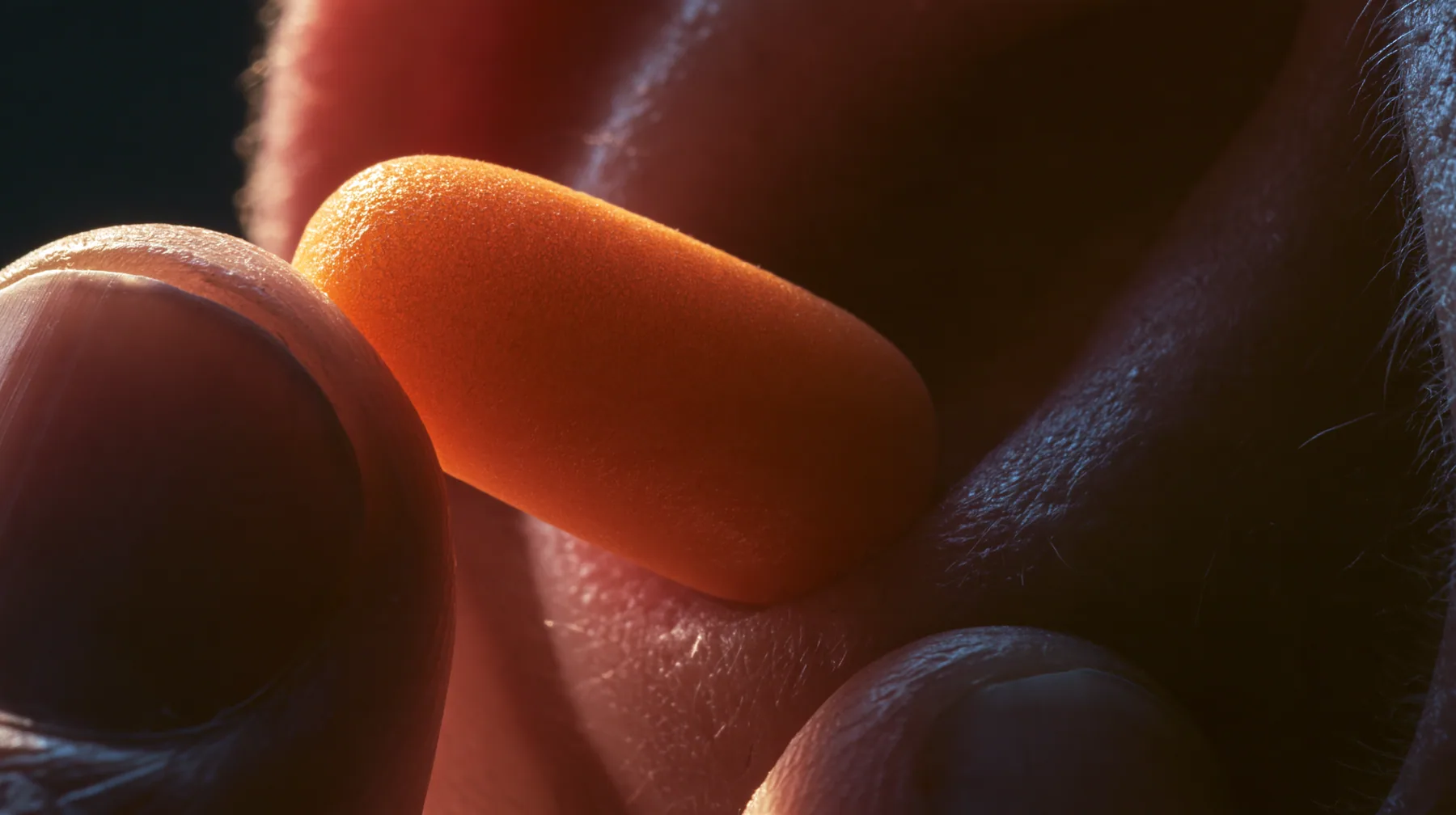 macro of two fingers pulling an orange foam earplug out of an ear, macro product photograph, hard rim light, razor-thin focus, twilight, no text, no letters, no logos