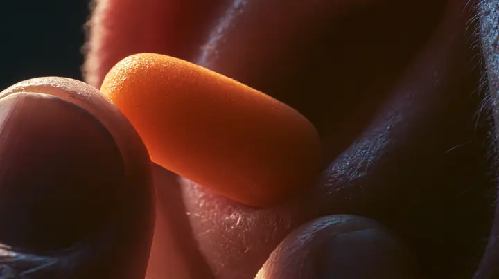 macro of two fingers pulling an orange foam earplug out of an ear, macro product photograph, hard rim light, razor-thin focus, twilight, no text, no letters, no logos