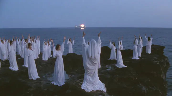 wide shot of hundreds of women in white gowns on black sea rocks raising their arms toward a passing ship, deep blue twilight, the last gold on the horizon, glassy sea, cinematic 35mm film still, anamorphic, fine…