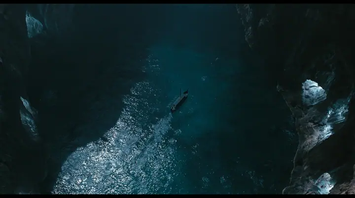 high aerial of the dark water of a narrow sea strait between two cliffs of lit alcoves, tiny swimmers far below drawn toward the cliffs, a long black ancient Greek galley with a single mast, a square sail and two…