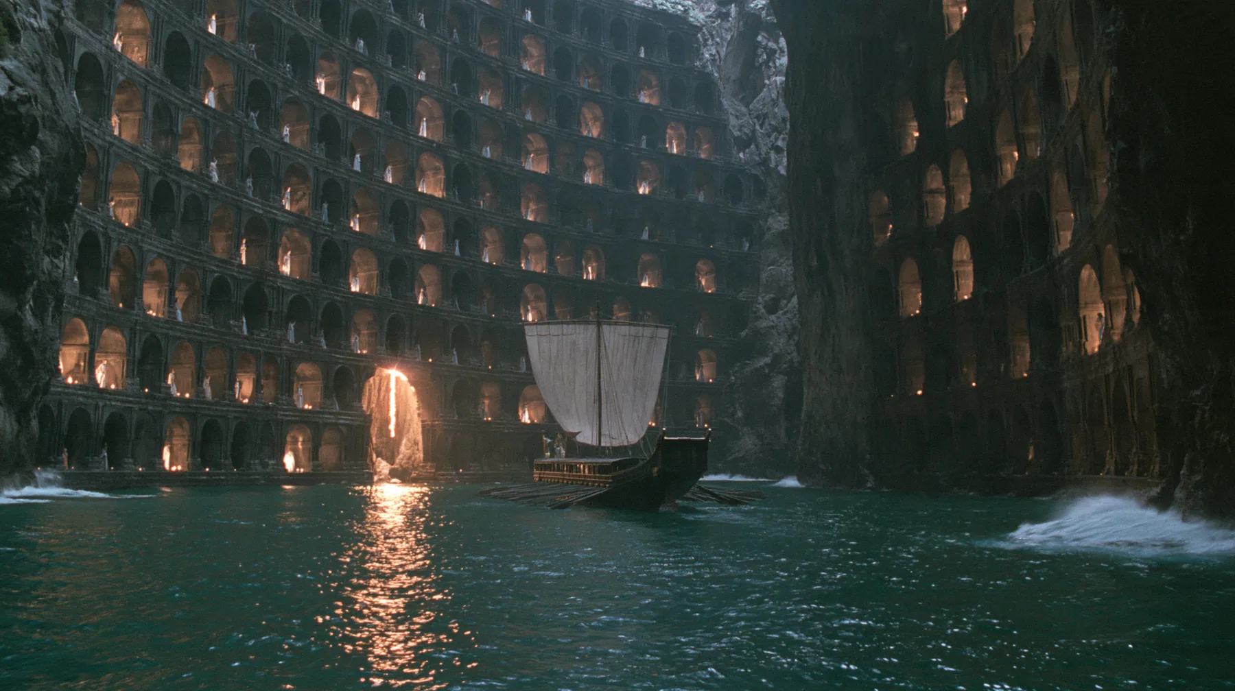 extreme wide shot of a long black ancient Greek galley with a single mast, a square sail and two banks of oars entering a narrow sea strait between two sheer black cliffs hundreds of metres high, the cliff faces…