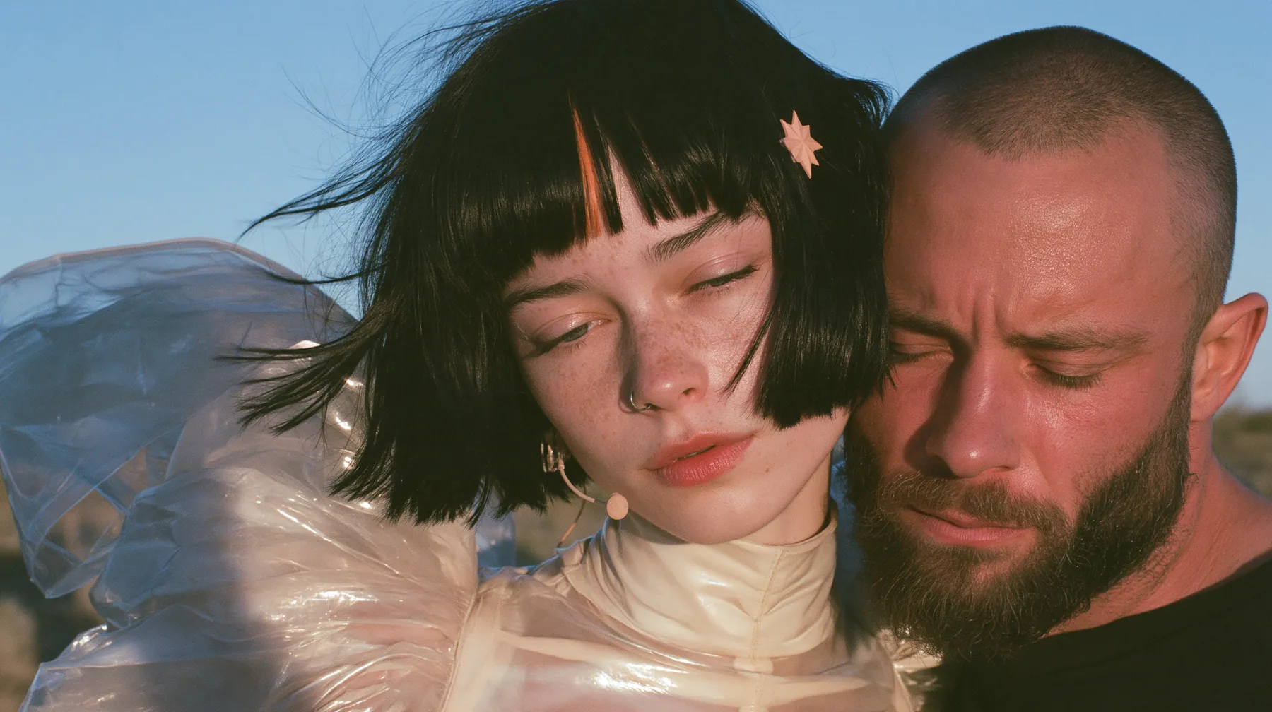 close-up of a Caucasian American woman in her mid-twenties with pale skin and light freckles, a glossy black blunt jaw-length bob with heavy straight bangs and one clay-orange streak through the bangs, a small flat…