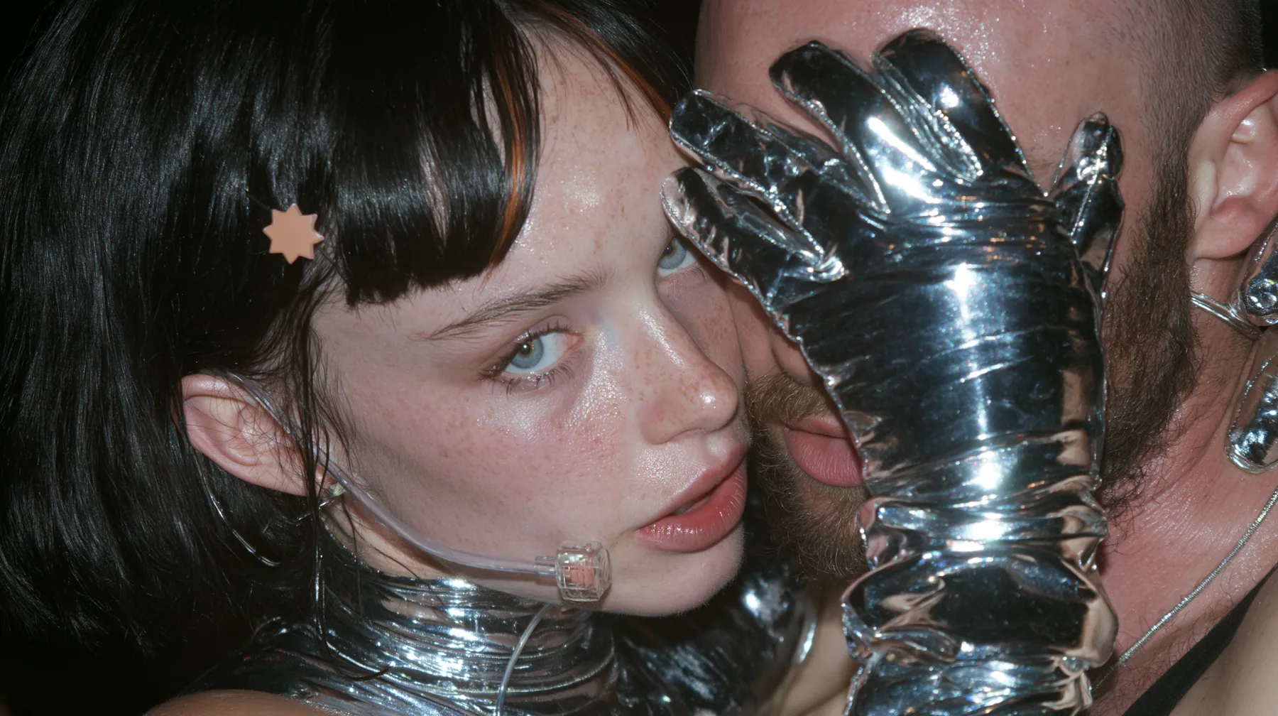 extreme close-up of a Caucasian American woman in her mid-twenties with pale skin and light freckles, a glossy black blunt jaw-length bob with heavy straight bangs and one clay-orange streak through the bangs, a…