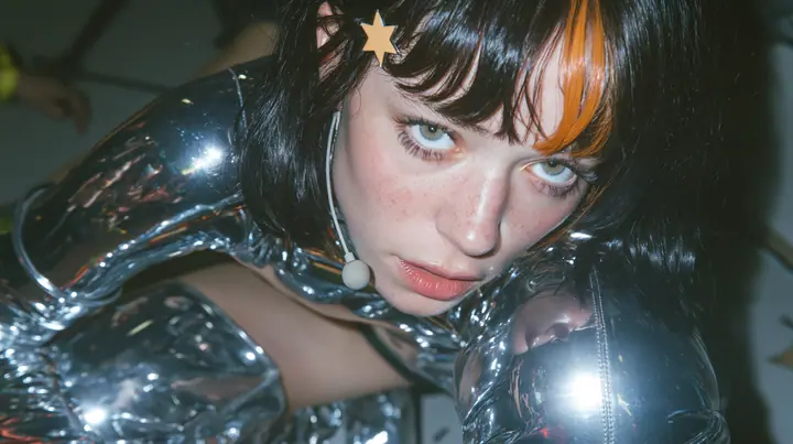 full-length shot of a Caucasian American woman in her mid-twenties with pale skin and light freckles, a glossy black blunt jaw-length bob with heavy straight bangs and one clay-orange streak through the bangs, a…