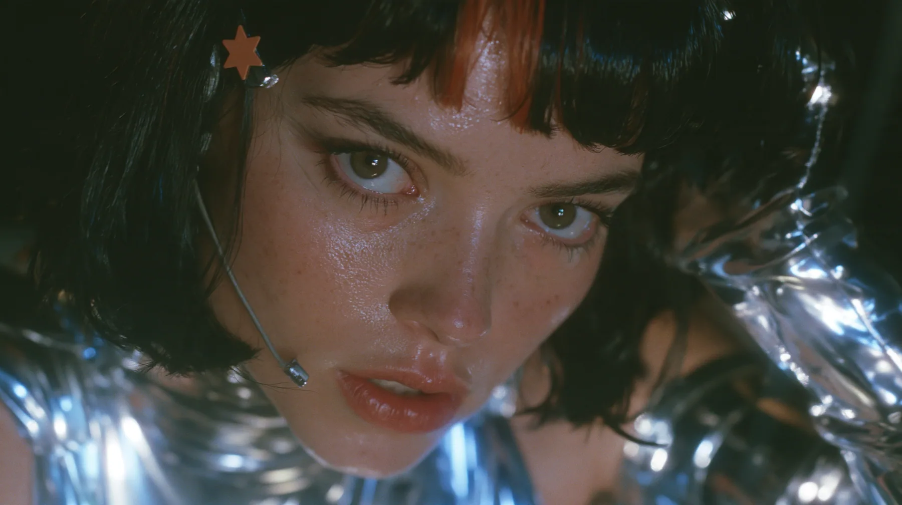 a Caucasian American woman in her mid-twenties with pale skin and light freckles, a glossy black blunt jaw-length bob with heavy straight bangs and one clay-orange streak through the bangs, a small flat clay-orange…