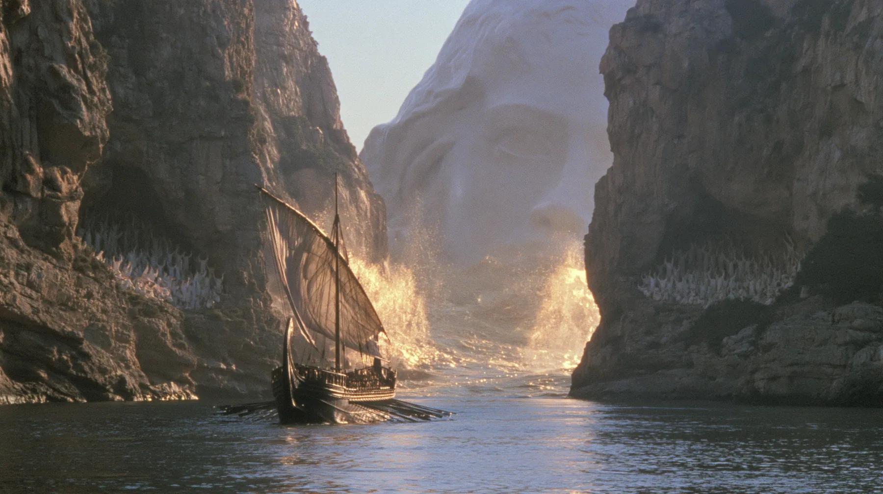 extreme wide shot of a long black ancient Greek galley with a single mast, a square sail and two banks of oars passing between the last lit cliffs of a narrow strait, thousands of women in white raising their arms in…