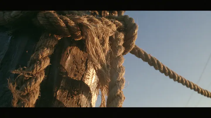 macro of hemp rope fibres fraying under strain around a wooden mast, sunrise, warm gold light and long shadows, spray lit gold, cinematic 35mm film still, anamorphic, fine grain, no text, no letters, no logos